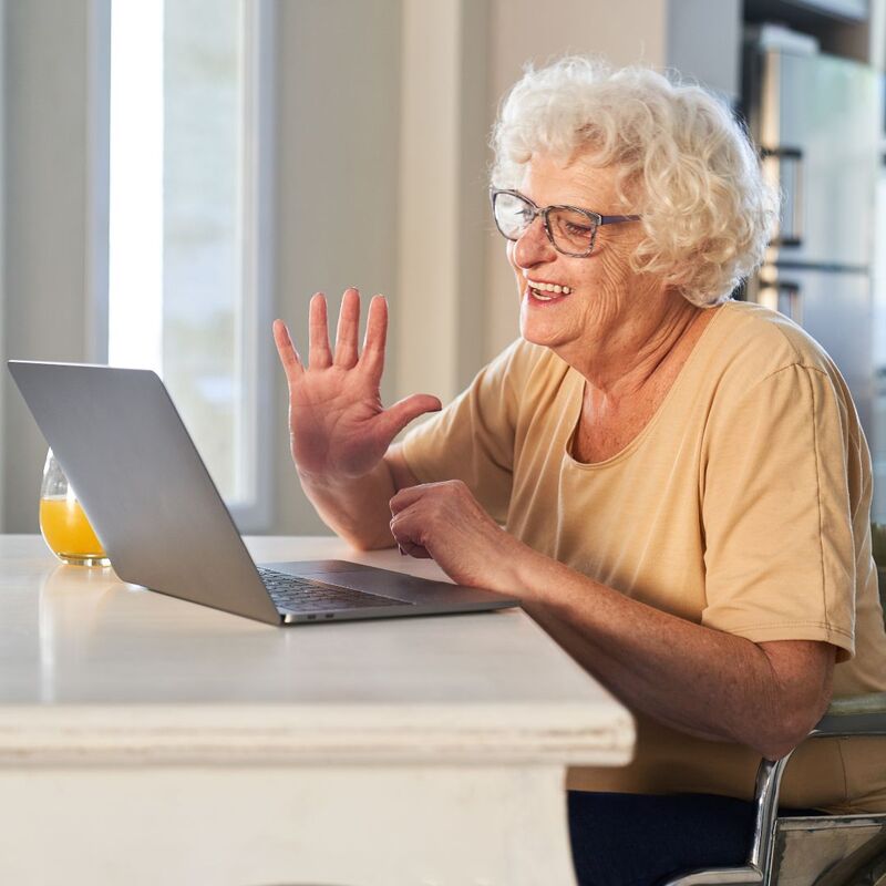 Photo of an older woman waving at her laptop.