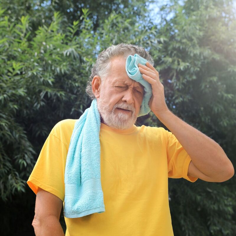 Photo of an older man pressing a towel to his own forehead, looking distressed in the heat.