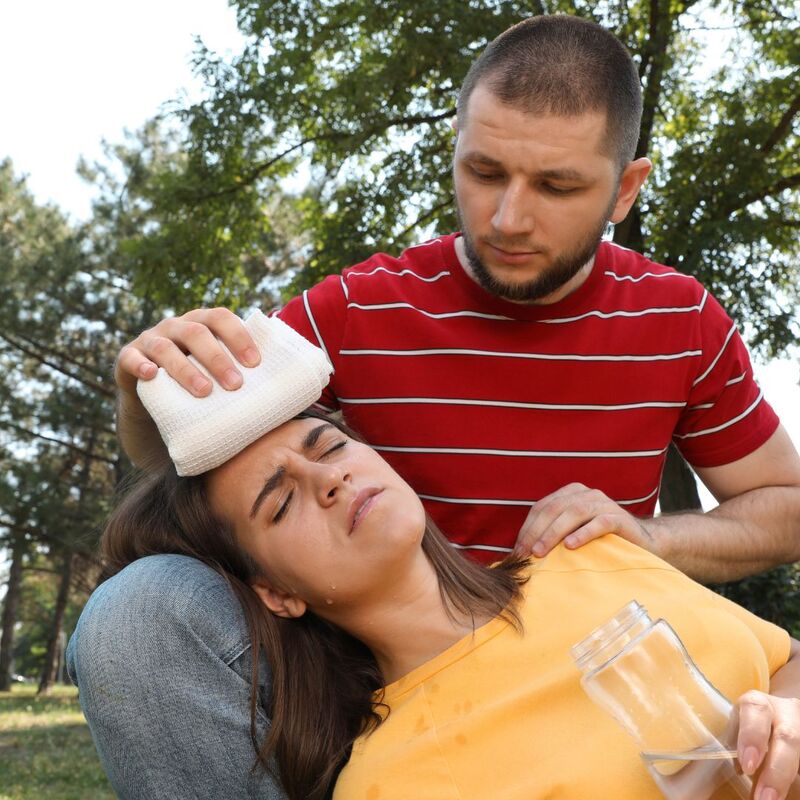 Photo of a woman laying down in distress while a man presses a cold cloth to her forehead.